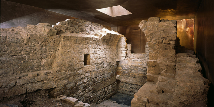 Foto: Innenansicht Mikwe © Peter Seidel Reste Mauerwerk von Mikwe, umgeben von bronzefarbenen Schutzbau